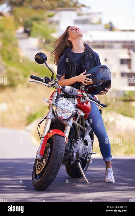 Letting her hair loose. A young woman sitting on her motorcycle ...