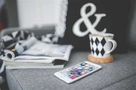 White mobile phone lying on a couch with cup and stack of magazines · Free Stock Photo