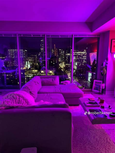 a living room with purple lighting and large windows overlooking the city lights at night time