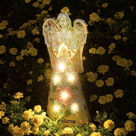 an angel statue surrounded by yellow flowers with lights on it's wings ...