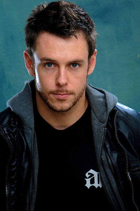 a man in a black shirt and jacket posing for a photo with a blue background