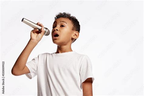 Portrait of little boy singing with microphone isolated on white backgroud. Human emotions ...