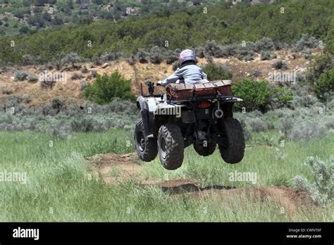 Motorcycle ATV ride on rough dirt track by man.Jumps over earth ramps. Wears a helmet for safety ...