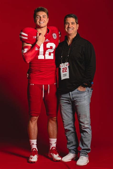 two men standing next to each other in front of a red background ...