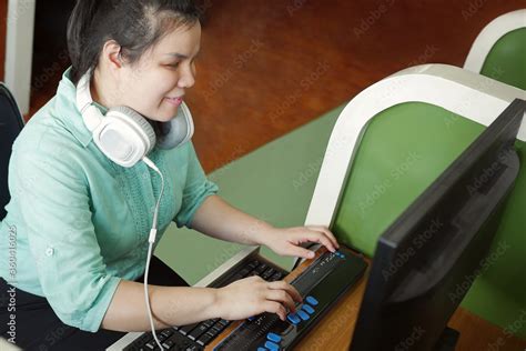 Asian young blind person woman with headphone using computer with refreshable braille display or ...