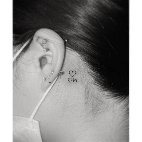 Tiny heart and initials tattoo located behind the ear.