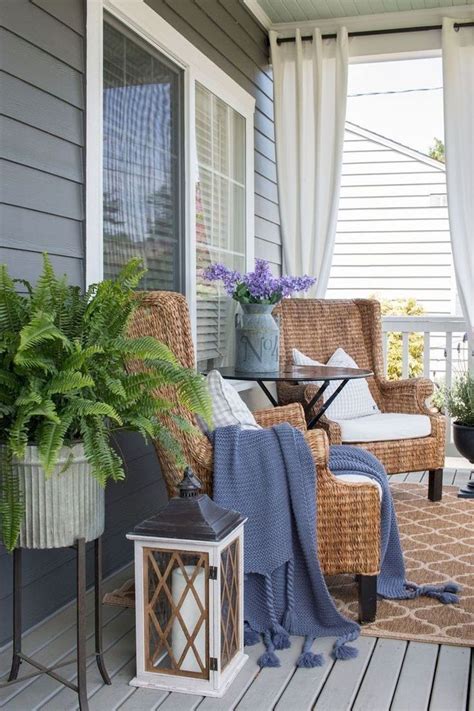 a porch with wicker chairs and potted plants on the front porch, covered by curtains