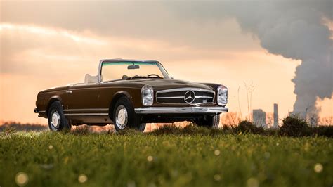 a brown mercedes 300sl convertible parked on top of a lush green field ...