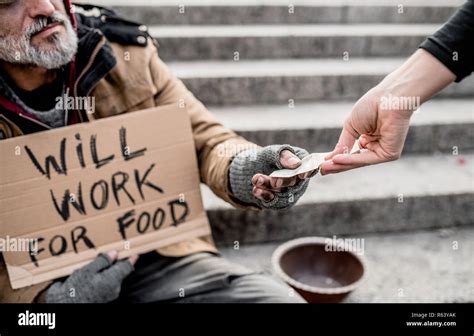 A midsection of woman giving money to homeless beggar man sitting in city Stock Photo - Alamy