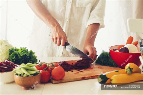 Woman chopping vegetables in a kitchen with knife in hand over chopping board — delicious ...