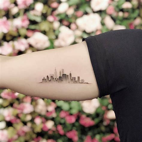 a woman's arm with a city skyline tattoo on the left side of her arm