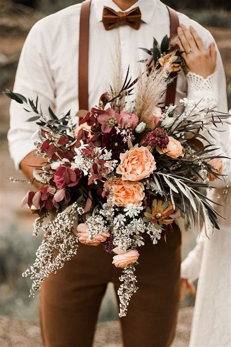 a man holding a bouquet of flowers and greenery in his hands while ...