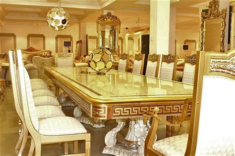 an ornate dining room table surrounded by white upholstered chairs and gold trimmings