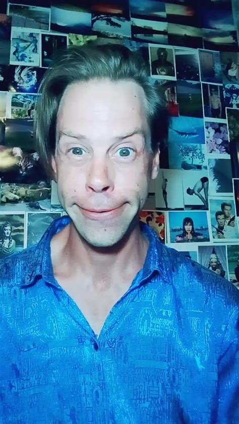 a man in blue shirt standing next to a wall with pictures on it and looking at the camera