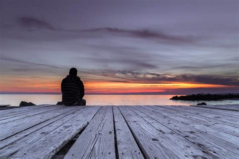 Man sitting on the pier and watching the sunset - The Thayer Institute