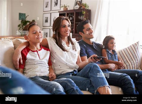 Young Hispanic family sitting on the sofa at home watching TV togther ...