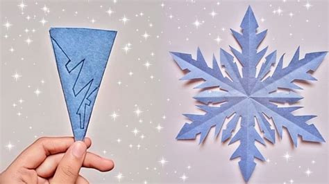 a hand holding an origami snowflake next to a paper cutout