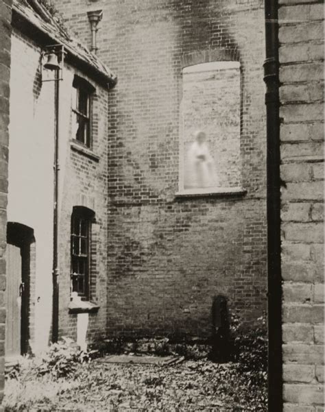 black and white photograph of an old brick building with a window on the side, in front of it