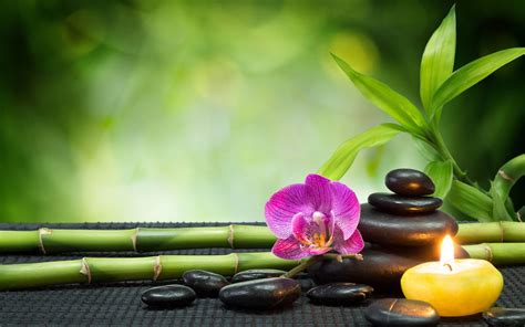 a candle and some rocks on a table with bamboo sticks, orchids and candles