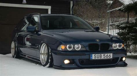 a blue car parked in front of a house covered in snow with its lights on