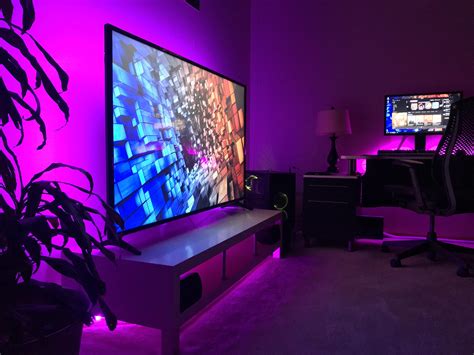 a living room with purple lighting and two monitors on the wall in front of it