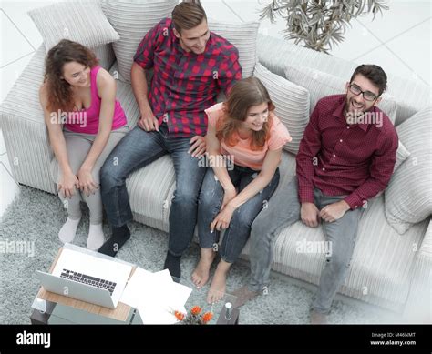 triumphant group of friends laughing while sitting on the couch in the living room Stock Photo ...