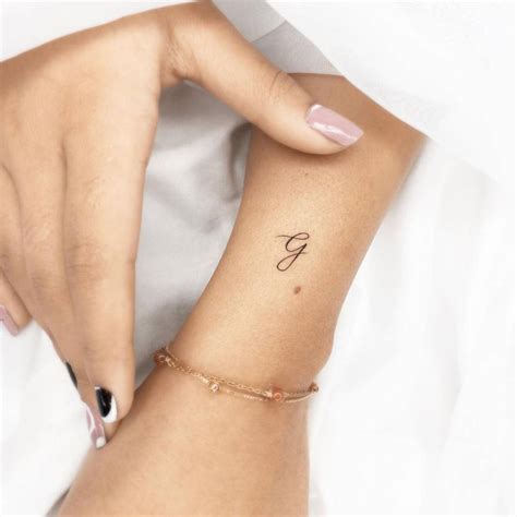 Minimalist letter "G" tattoo on the wrist.