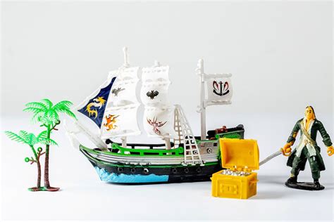 A tiny toy pirate ship with a treasure chest and a statue of a pirate on white background ...