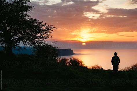 Man Standing On Cliff Watching The Sunset Over The Sea | Stocksy United