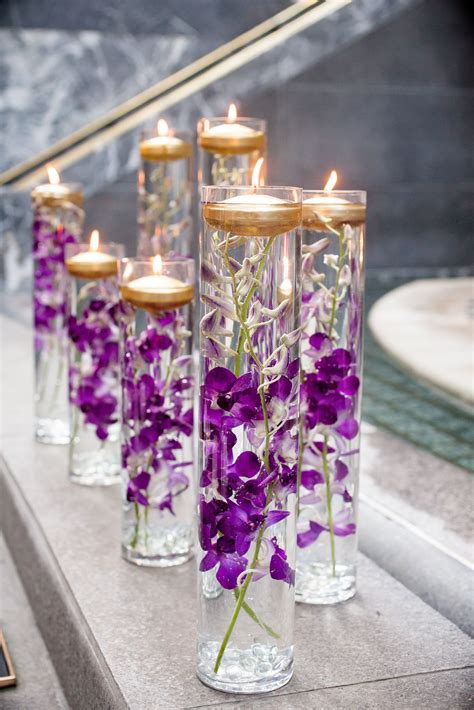 Glass vases were filled with purple orchids and floating gold candles for a… | Wedding flower ...