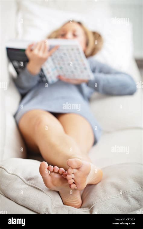 Barefoot young woman lying on sofa and reading book, shallow depth of field, focus on foot soles ...