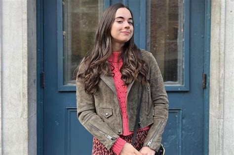 a woman standing in front of a blue door wearing a pink sweater and leopard print skirt