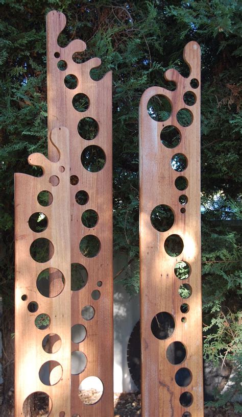 two wooden sculptures with holes in them sitting on the ground next to ...