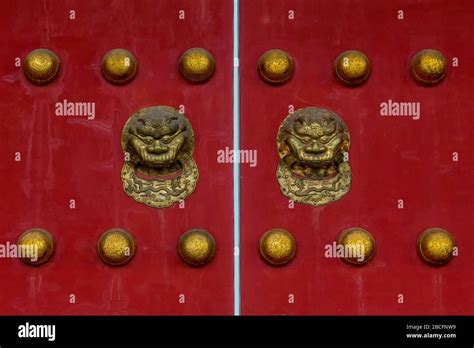 Ornate gold colour lion heads and studs fixed to a pair of red doors in The Forbidden City ...