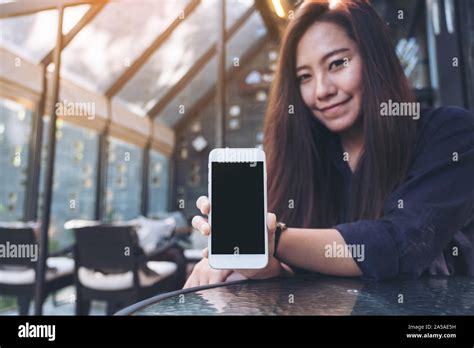 Mockup image of a beautiful asian woman holding and showing white mobile phone with blank black ...