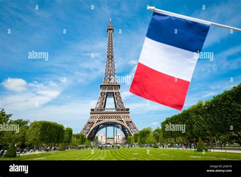 French flag flying in bright blue sky in front of the Eiffel Tower in ...