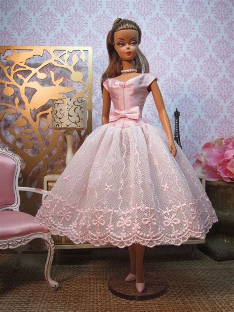 a doll in a pink dress is standing next to a chair