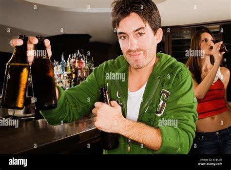 Young man holding a beer bottle at a bar counter with a young woman drinking behind him Stock ...