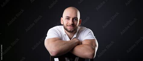 turkish student man with bald head and white polo shirt lean on chair back with arms crossed ...