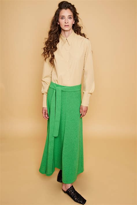 a woman standing in front of a beige wall wearing a green skirt and black shoes