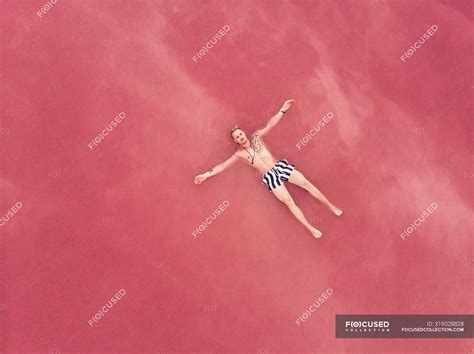 Top view of resting male in swimwear floating on surface of salty pink water of exotic lake in ...