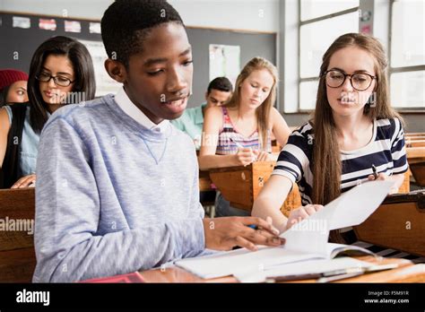 Two students sitting at desk in classroom, helping each other with Stock Photo: 89571267 - Alamy