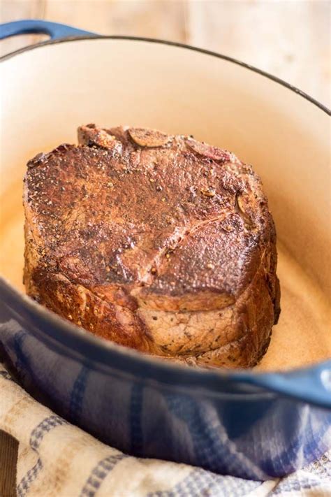 a steak in a skillet on a wooden table with a blue dish towel next to it