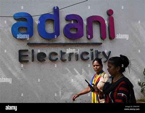 Women walk past the Adani electricity logo on the wall in Mumbai. Adani ...