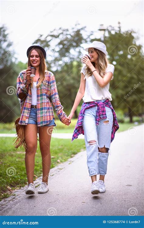 Dos Mujeres Jovenes Que Llevan a Cabo Las Manos Que Caminan En Parque Verde Mejores Amigos Foto ...