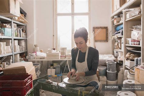 Caucasian woman is shaping pottery clay on a pottery wheel in a ceramic workshop. — indoor ...