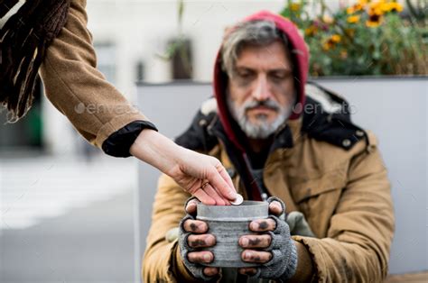 Unrecognizable woman giving money to homeless beggar man sitting in city. Stock Photo by halfpoint