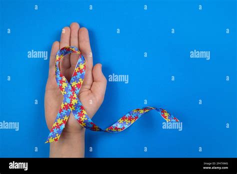 World Autism awareness day. Autistic boy hand holding puzzle pattern ribbon on blue background ...