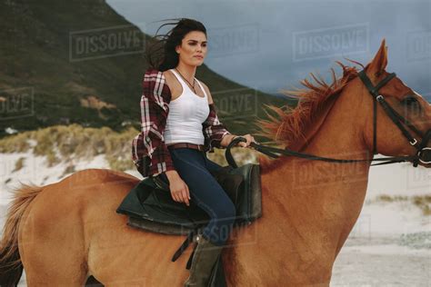 Attractive young woman riding a horse at the beach in evening. Cowgirl ...