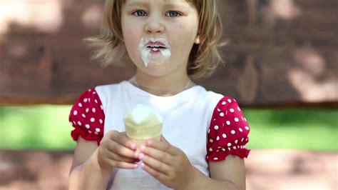 Little cheery girl sits on the swing bench eats ice cream and licks her ...